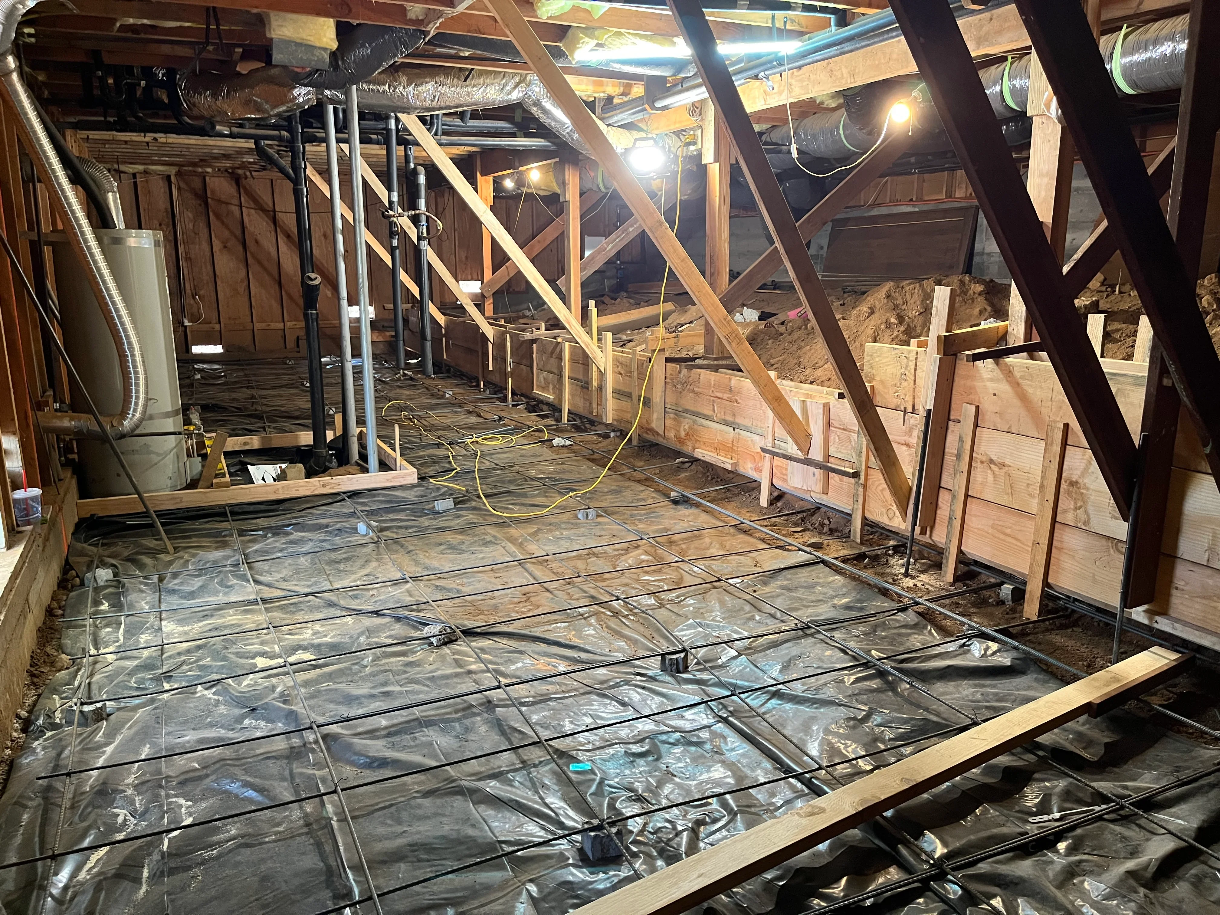 Basement framing with wood studs, joists, and black vapor barrier on floor