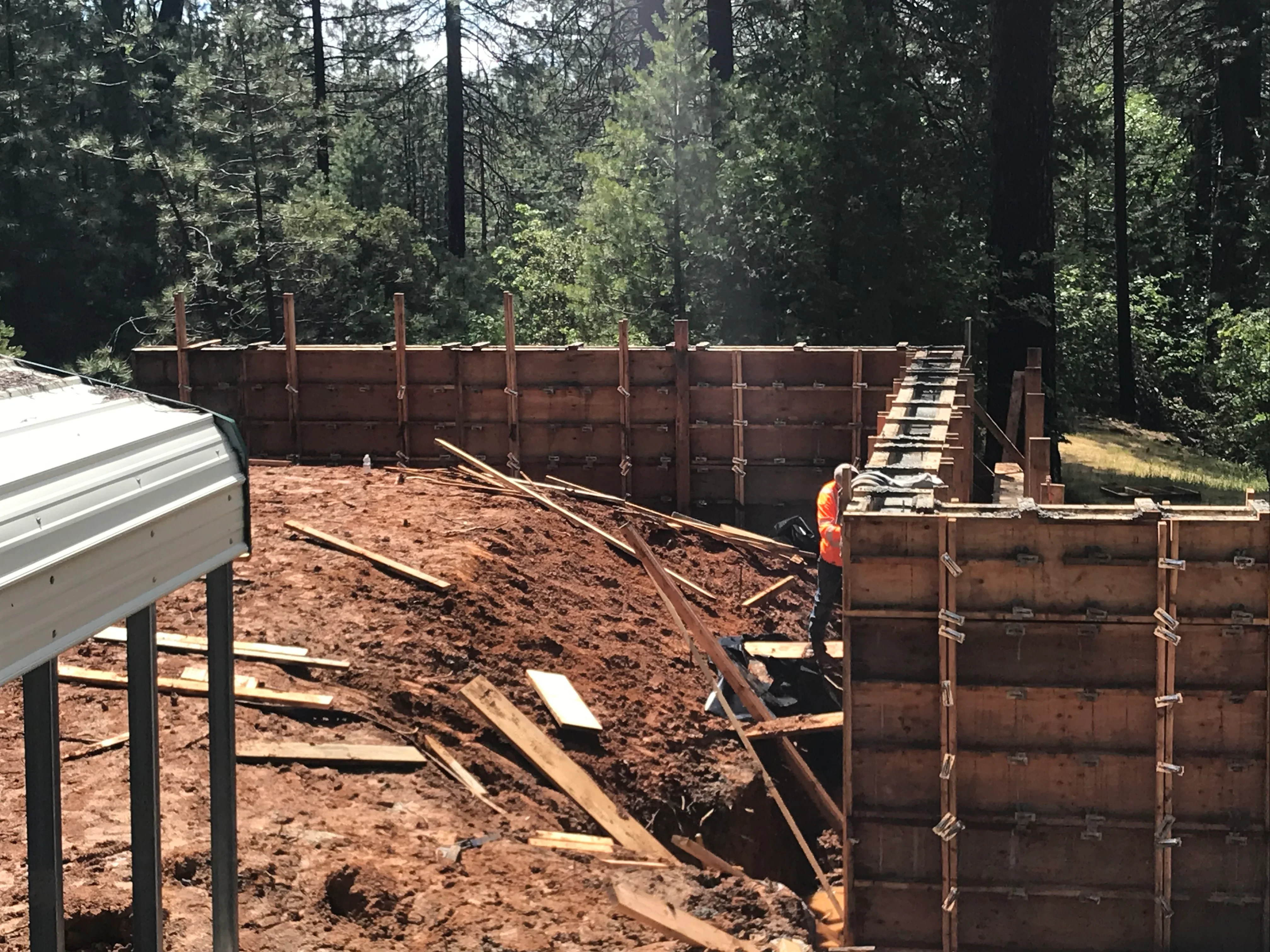 Timber retaining wall with vertical posts and cable bracing during construction, forested backdrop