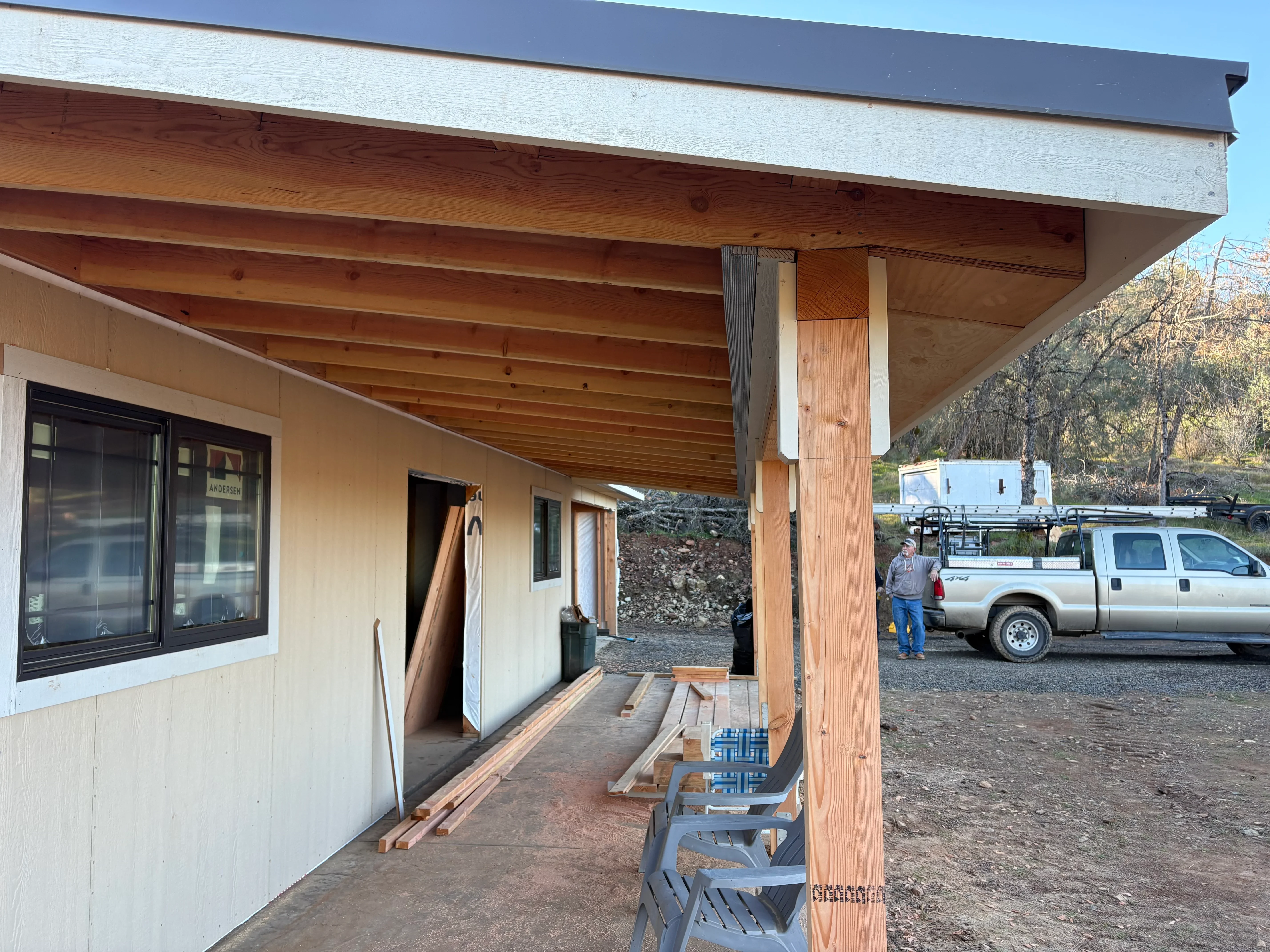 Covered porch with exposed wood beams, white fascia, and support posts under construction