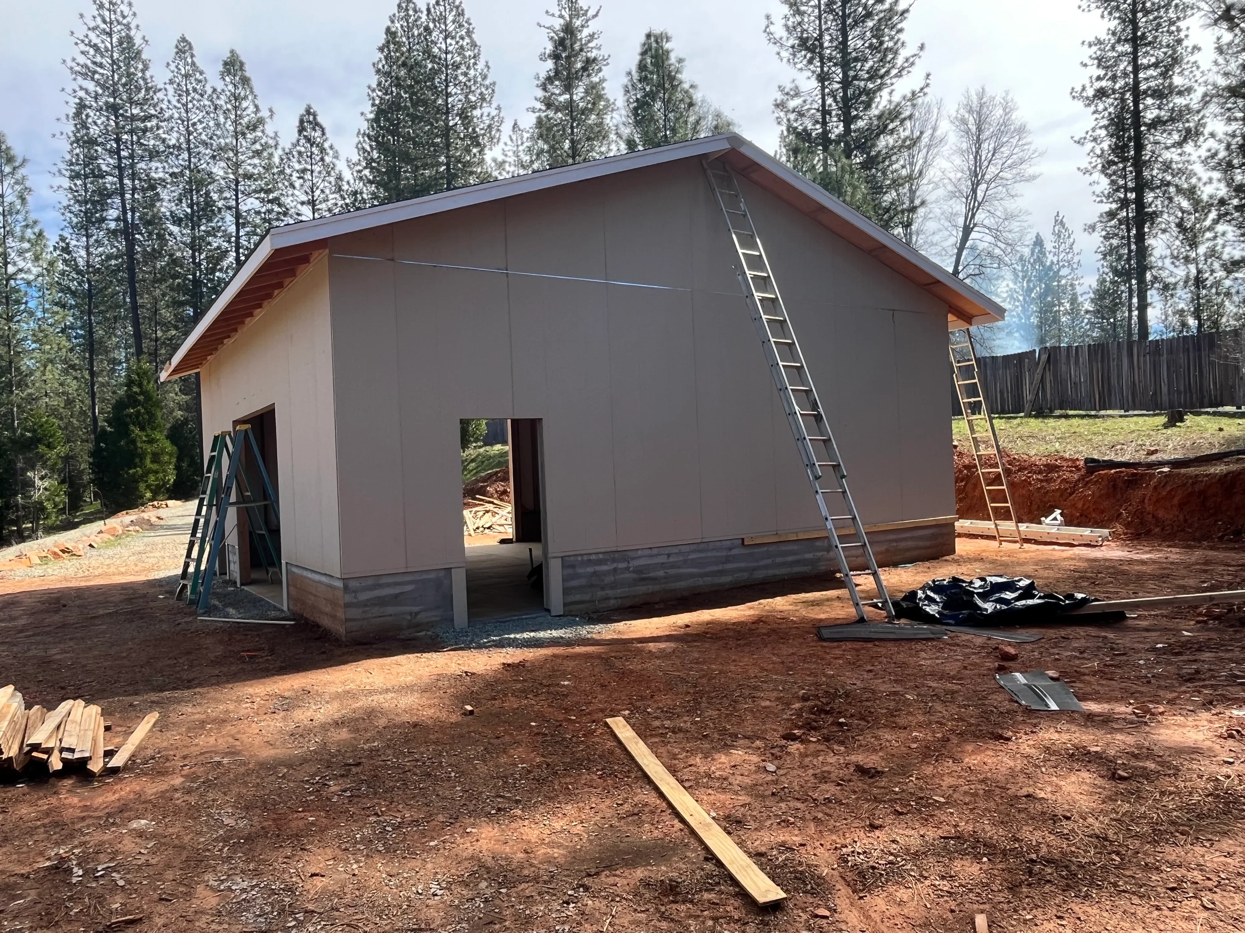 New residential building with pitched metal roof, wood framing, concrete foundation, and exterior wall sheathing during construction