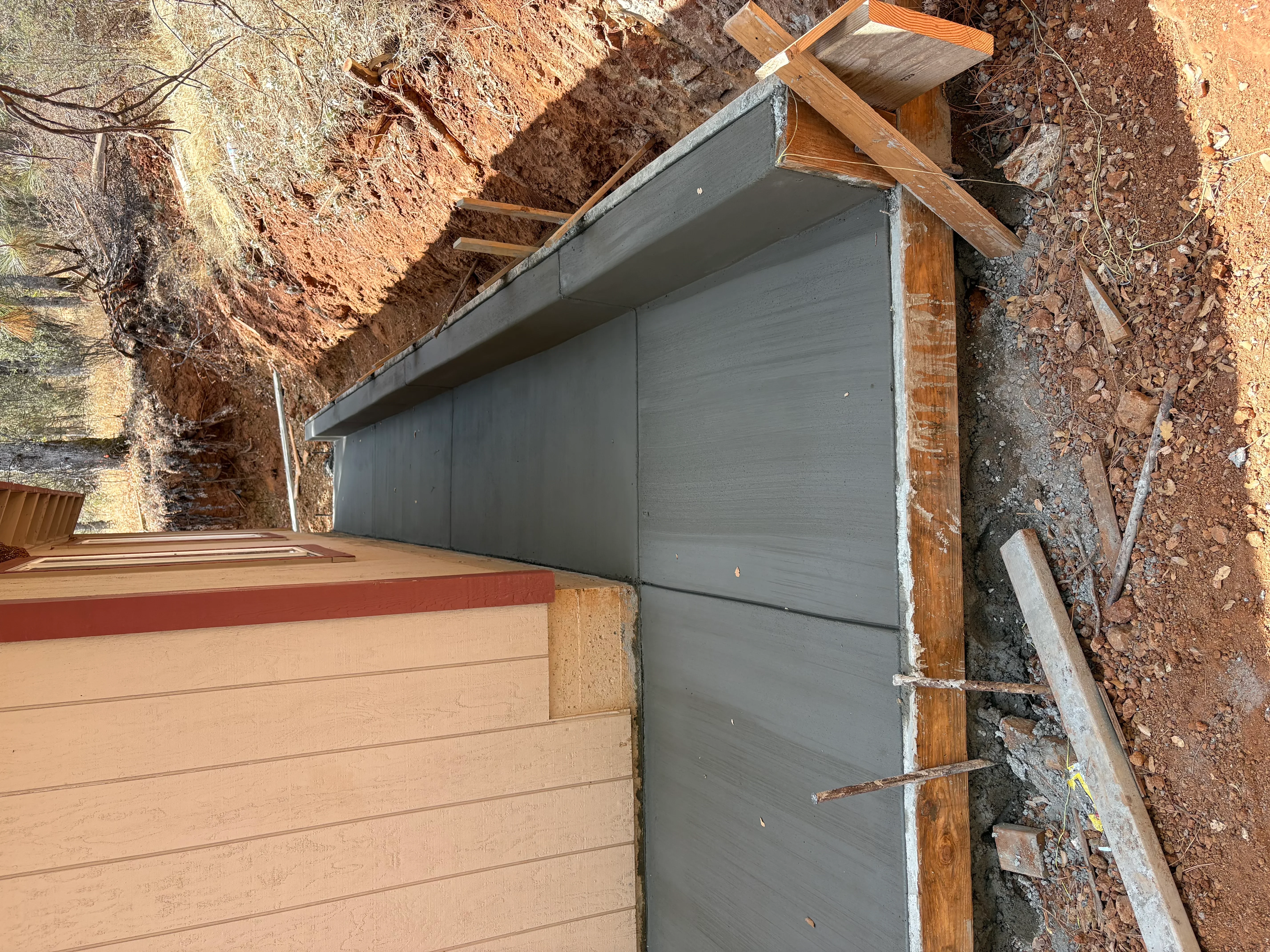 Gray sectional garage door installed on hillside with wooden frame support and concrete foundation