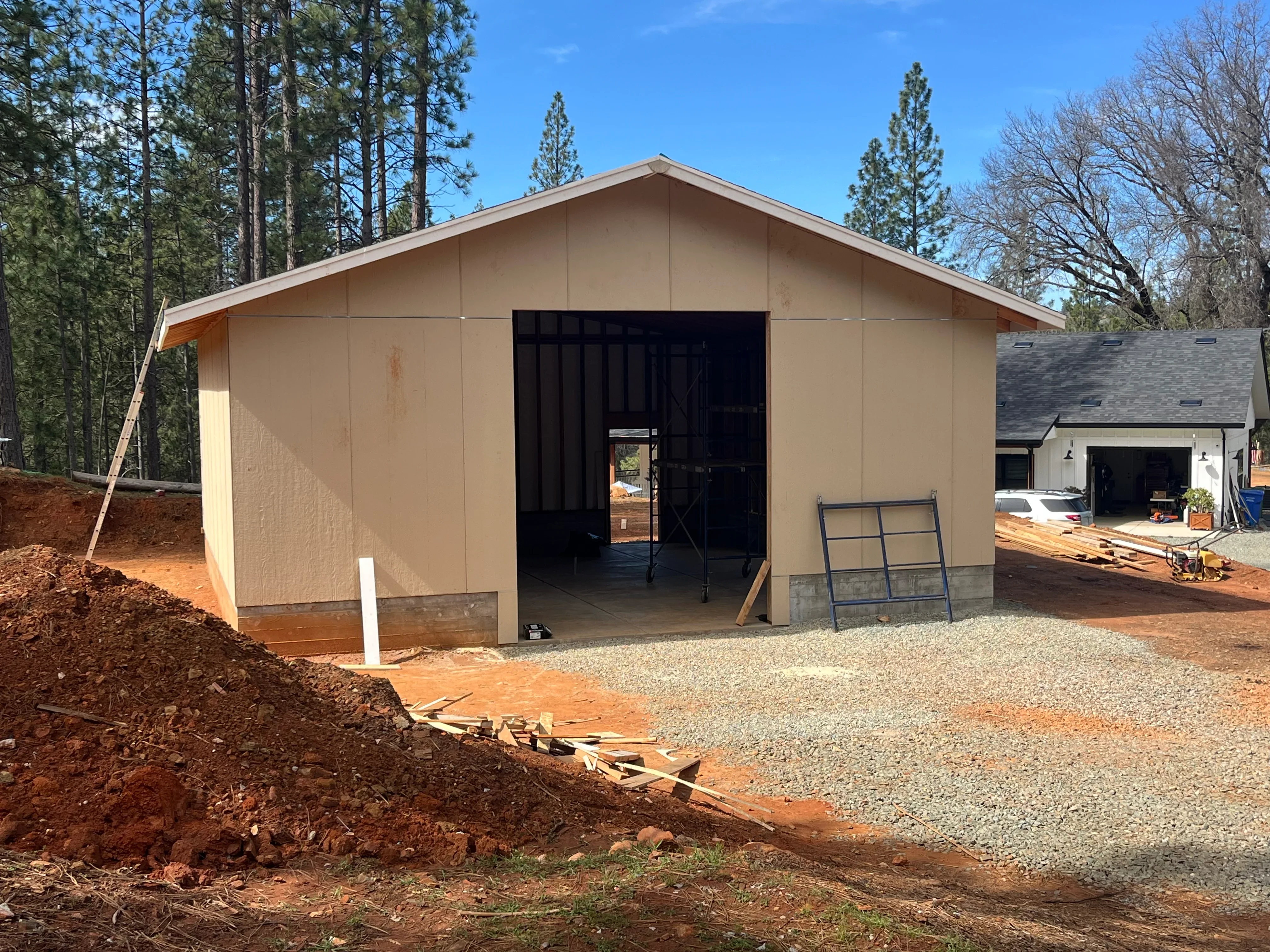 Tan gable building with black steel doors, concrete foundation, and gravel site work
