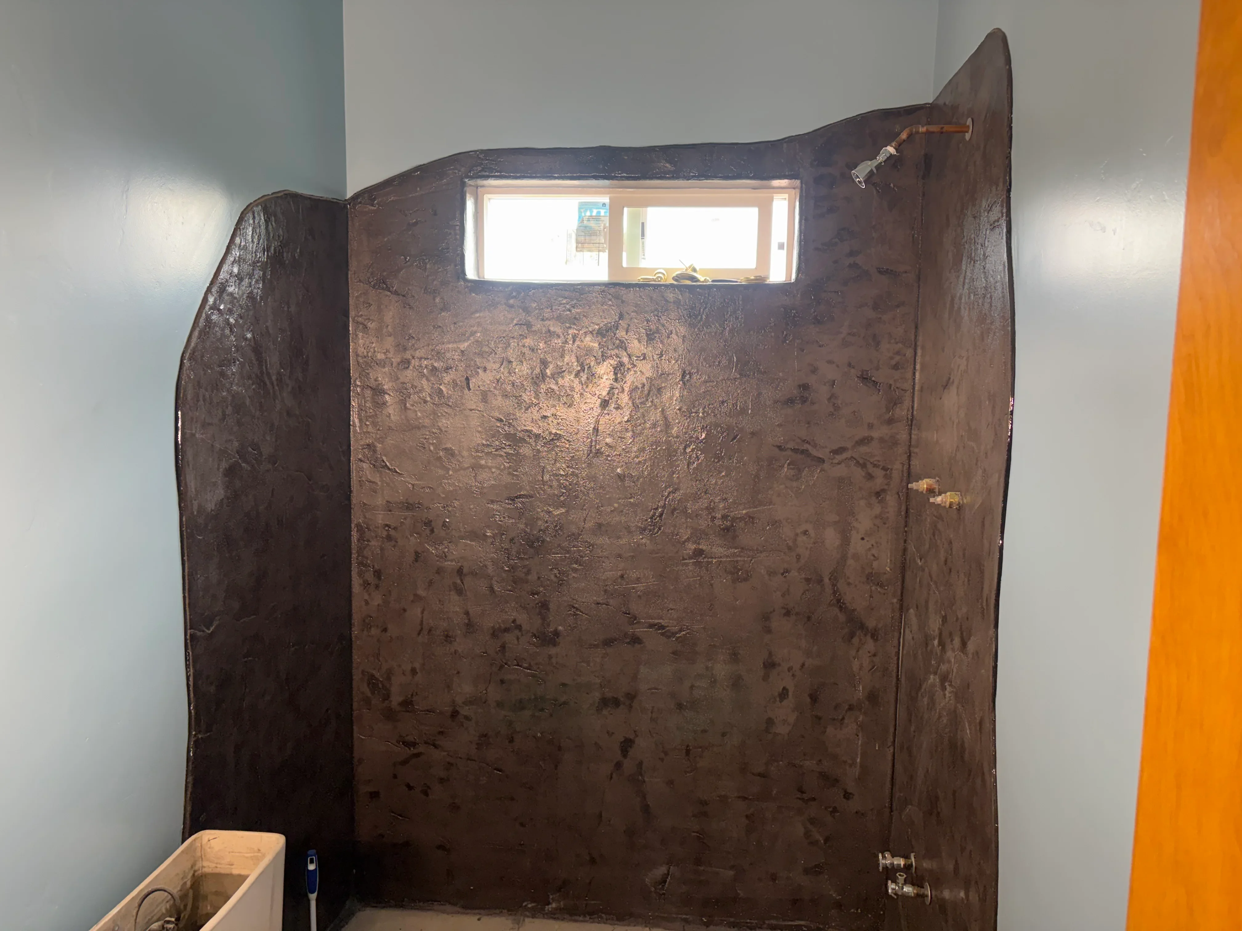 Dark metal shower enclosure with curved top and window opening, brass hardware and fixtures