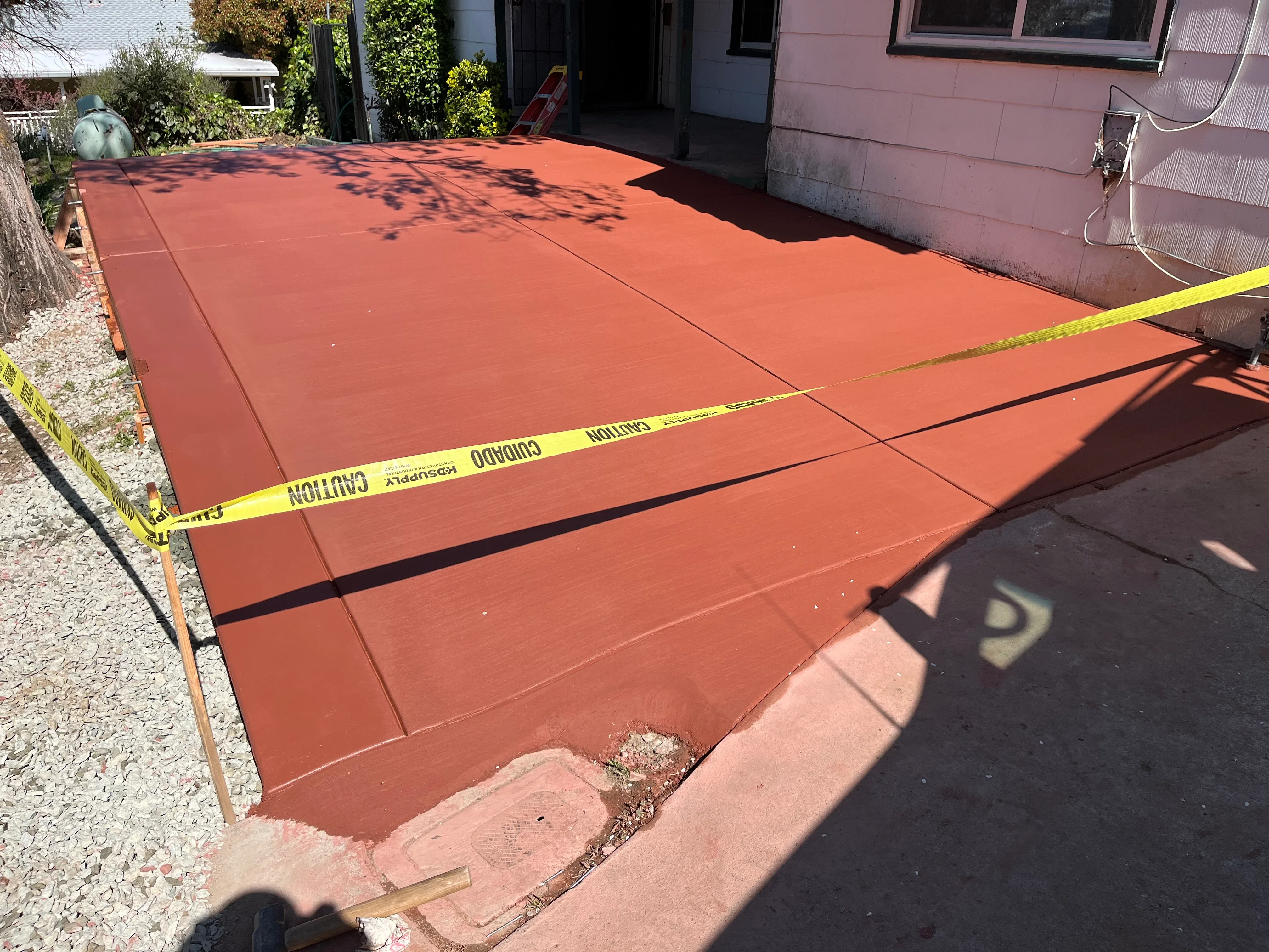 Newly poured red concrete patio with control joints and caution tape