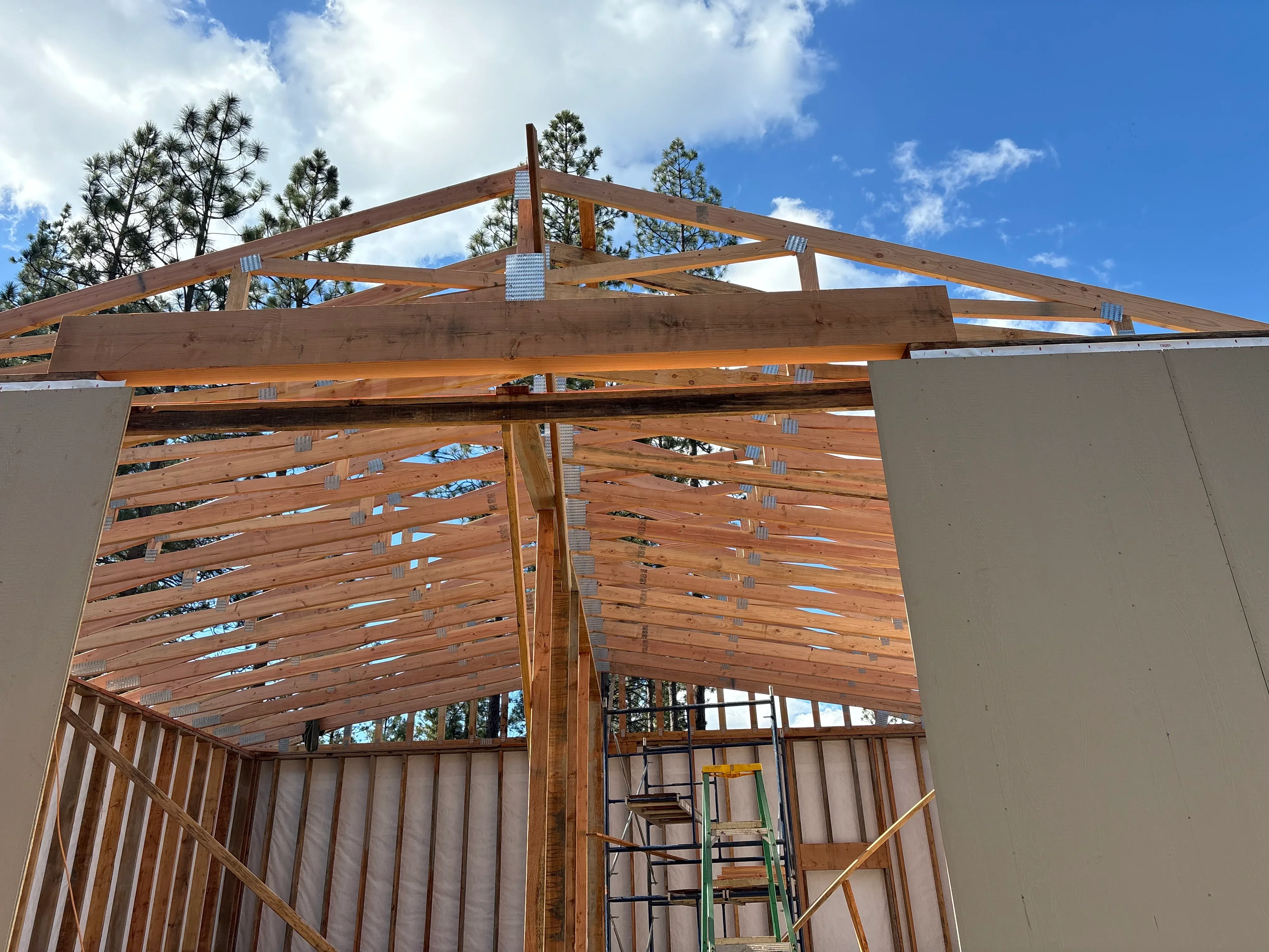 Timber frame roof structure with exposed wooden beams, trusses, and metal connectors during construction