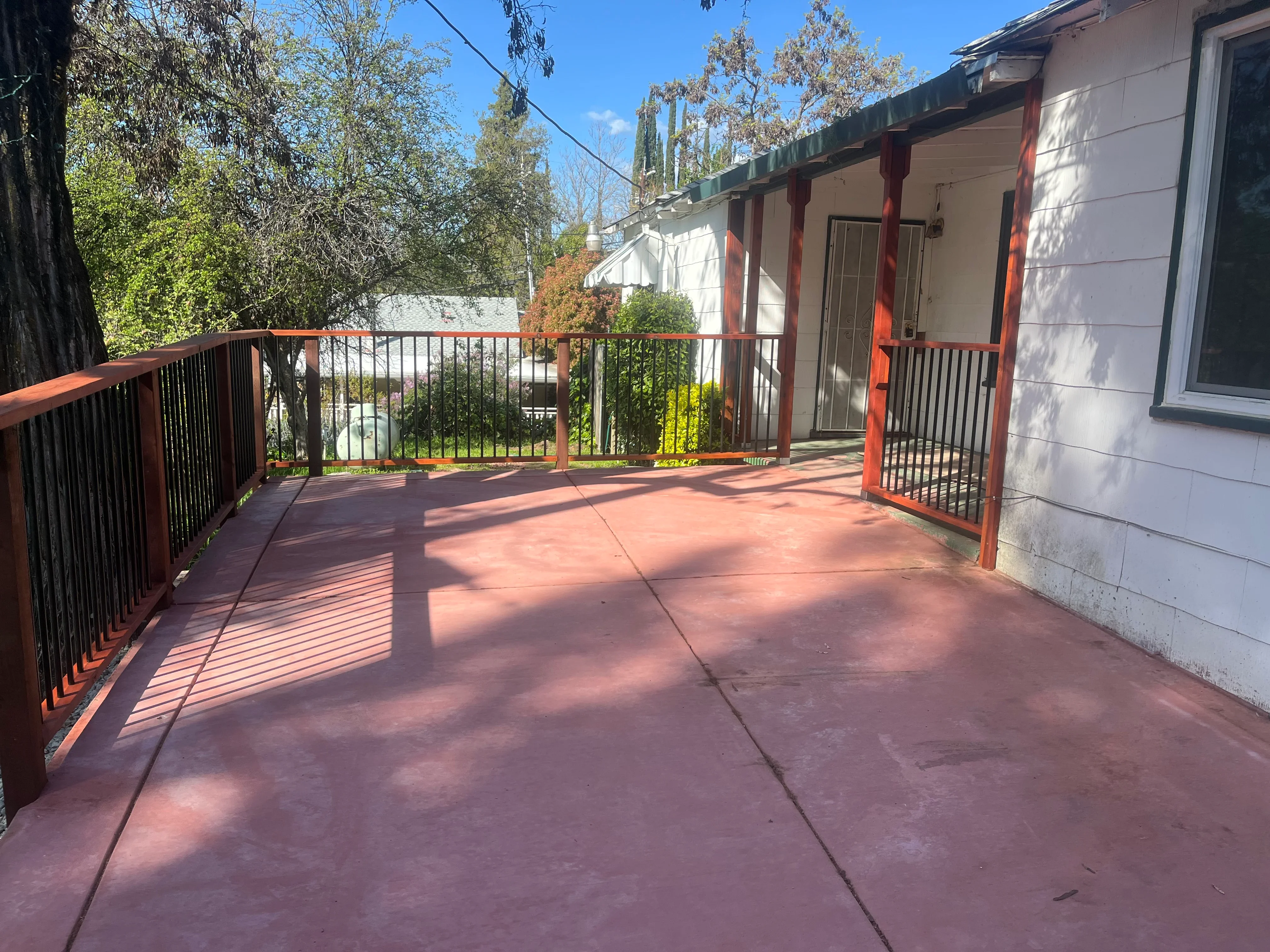 Redwood deck with red posts and black metal railing overlooking landscaped yard