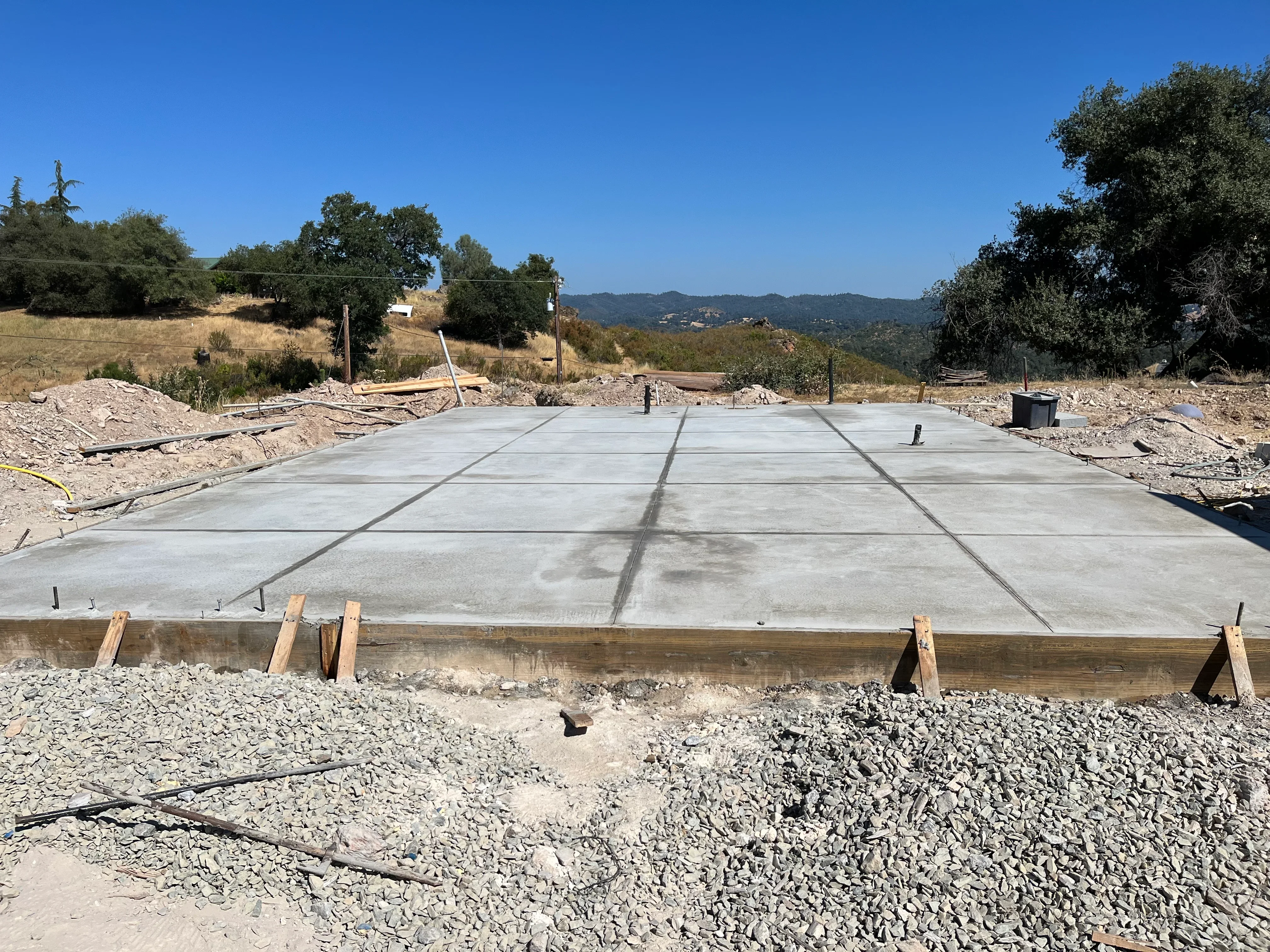 Finished concrete pad with control joints, timber frame, and gravel base on hillside property
