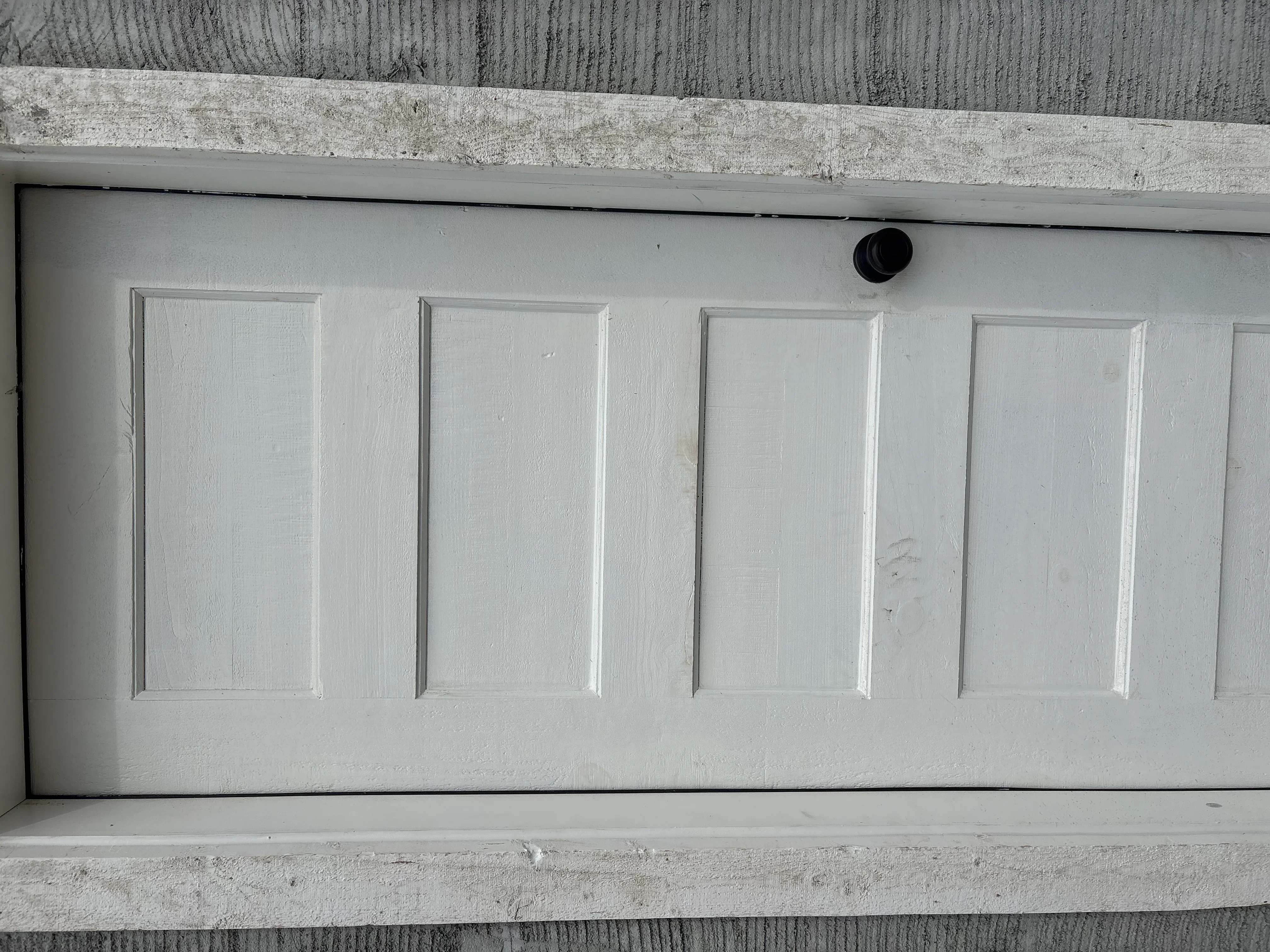 Four-panel white garage door with recessed panels and black hardware mounted in concrete frame