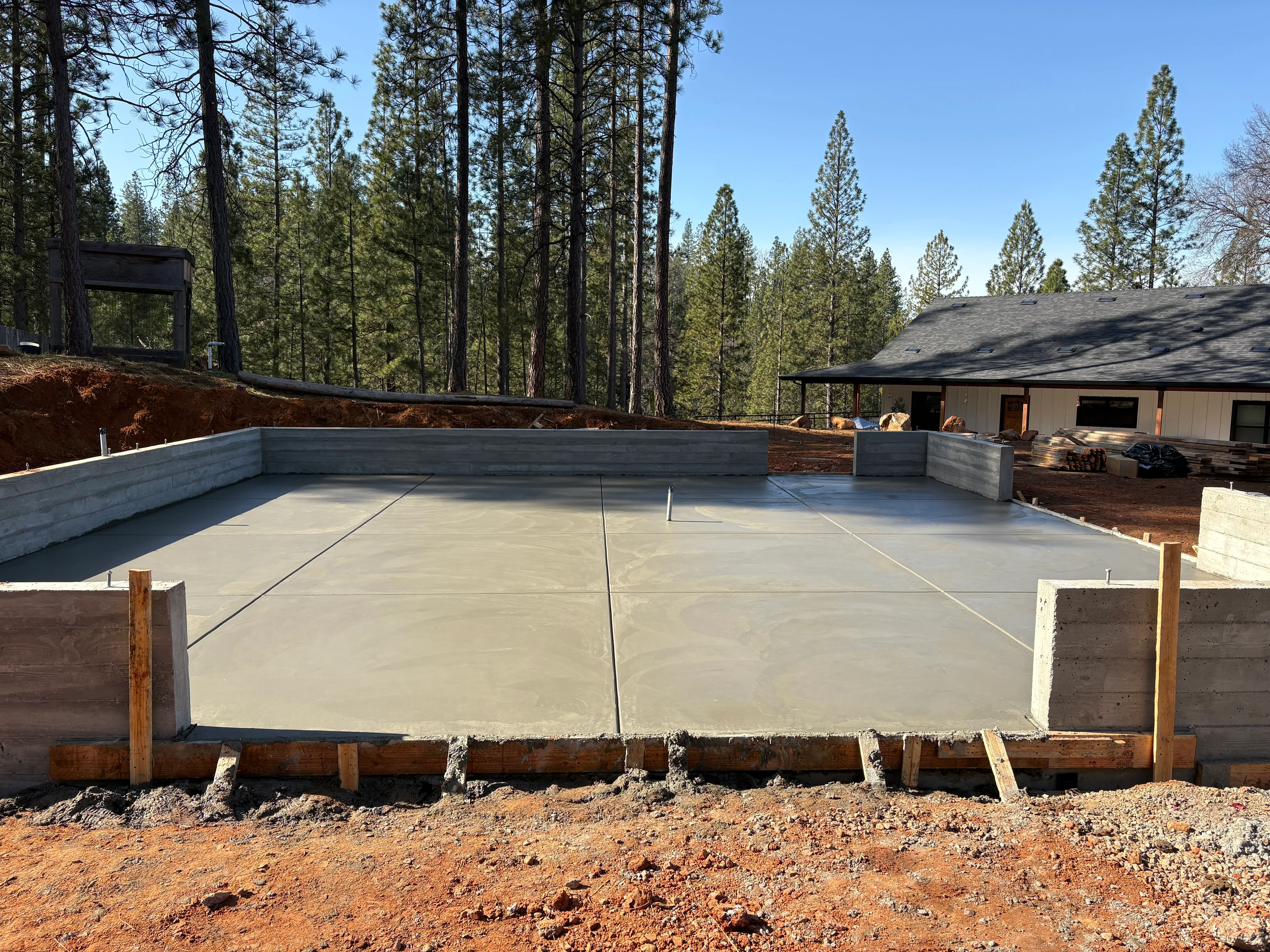 Newly poured concrete foundation slab with wooden forms and control joints in forest setting