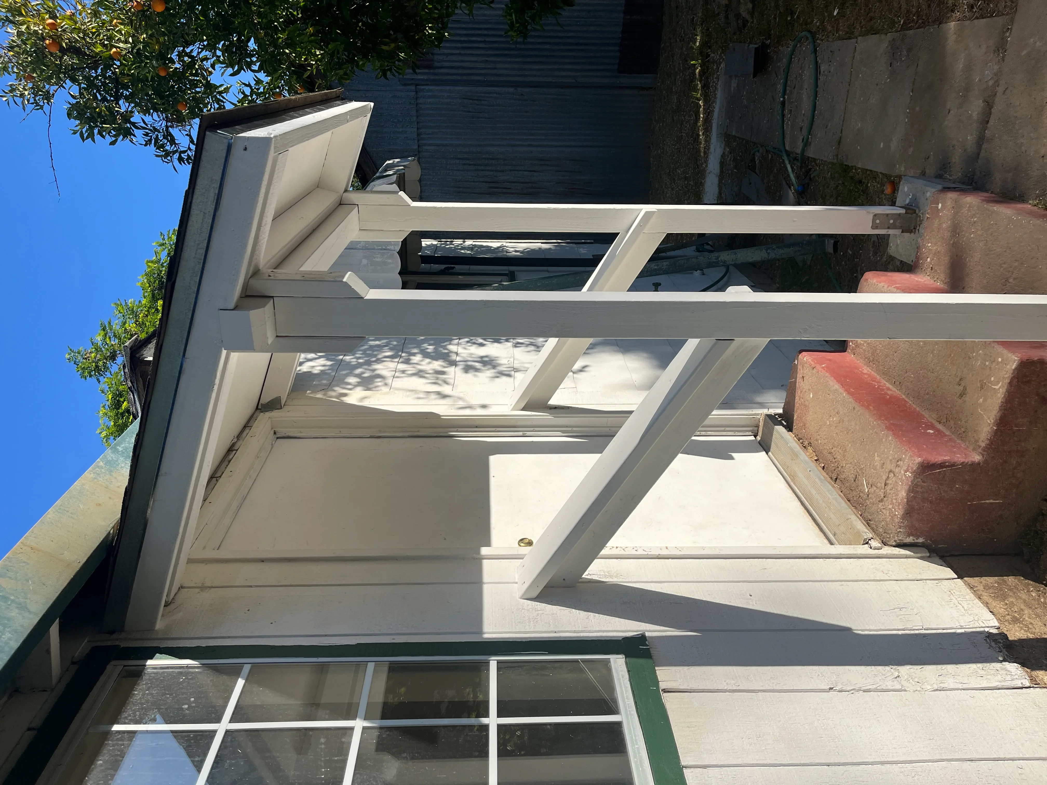 White vinyl pergola with cross beams attached to brick building, clear sky visible