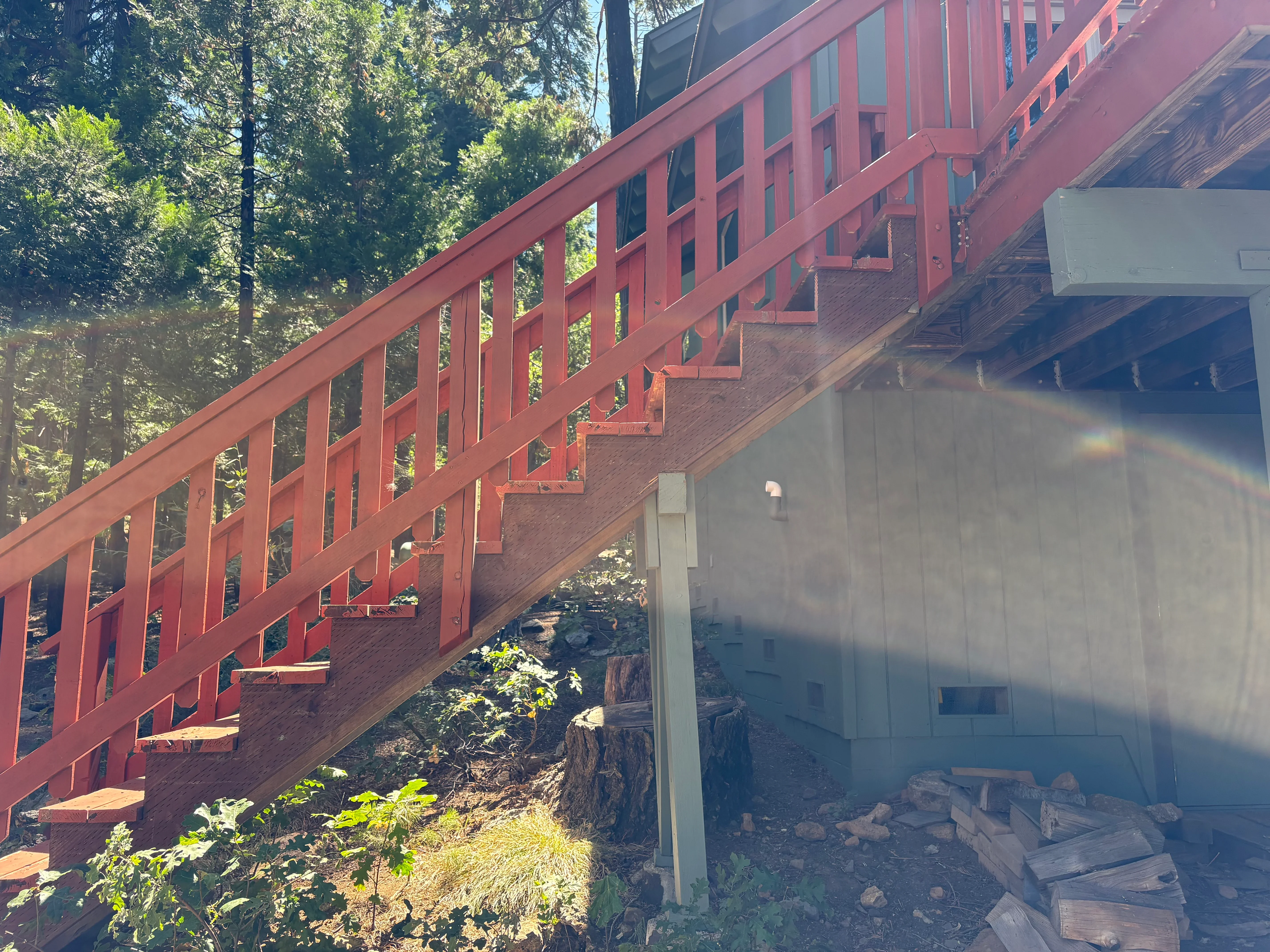 Red steel staircase with wood treads and lattice railings on hillside foundation